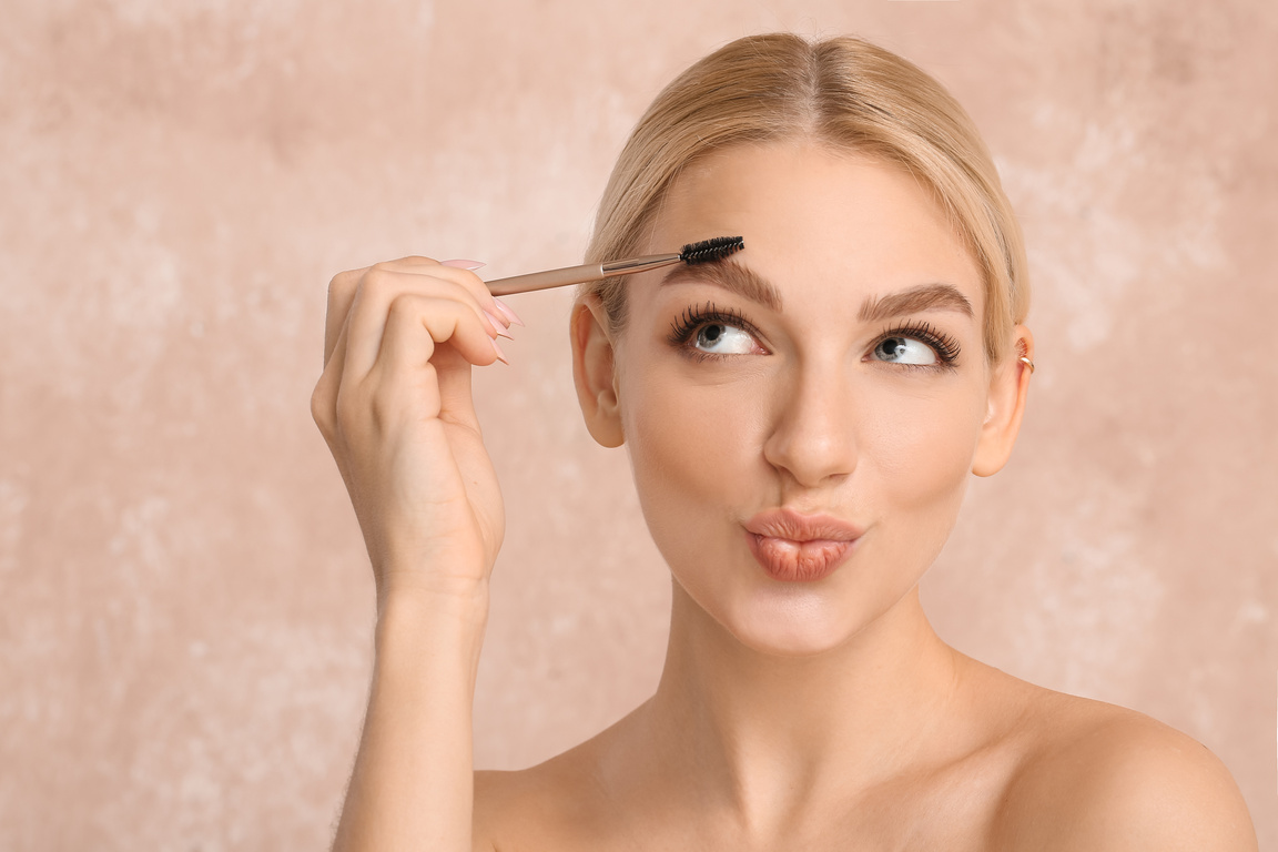 Young Woman Correcting Her Eyebrows on Color Background